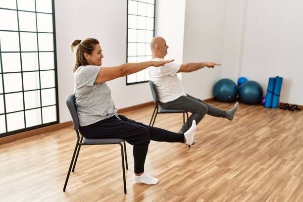 Two adults practicing seated leg and arm extensions in a chair yoga class