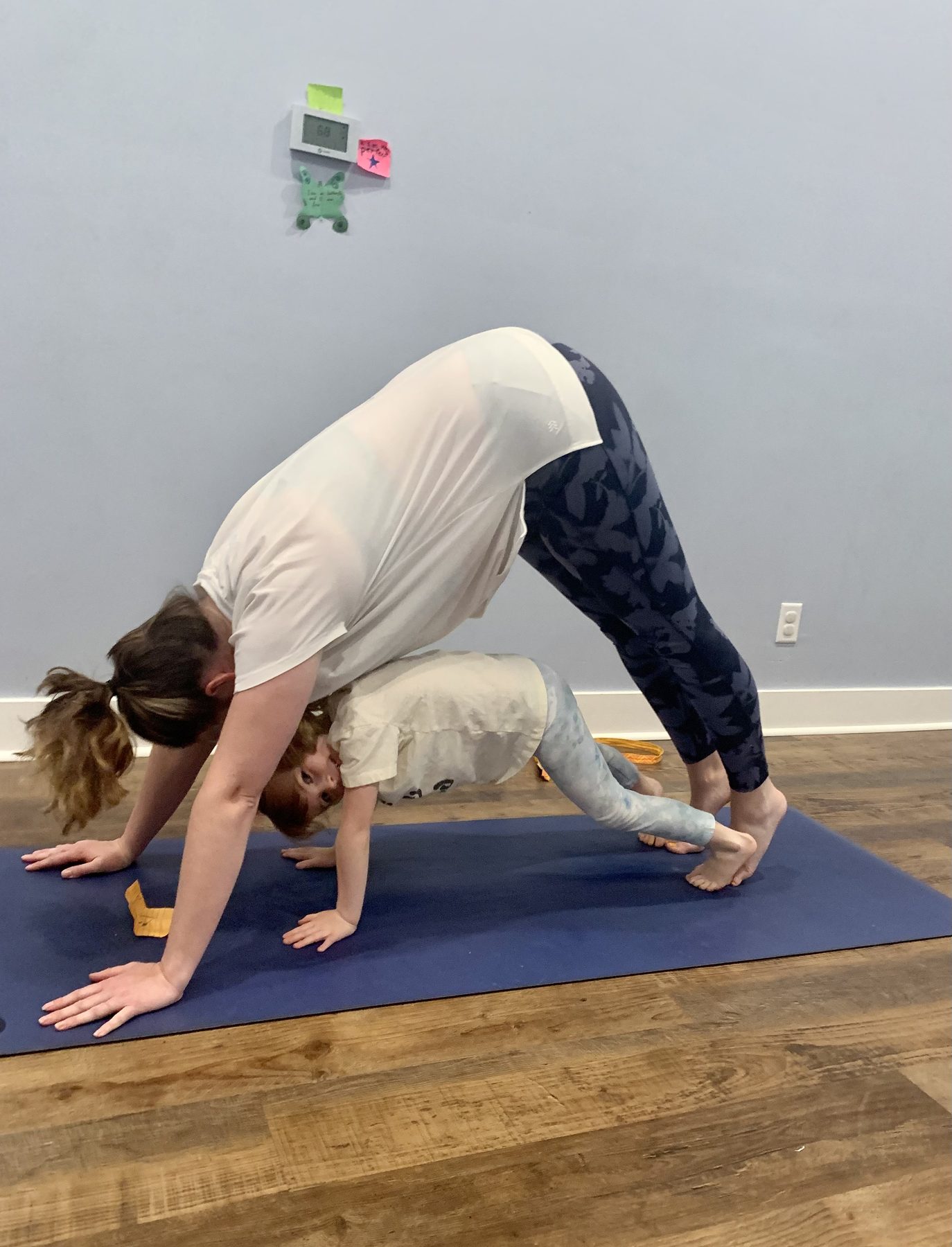 An adult and child practicing downward-facing dog together on a yoga mat